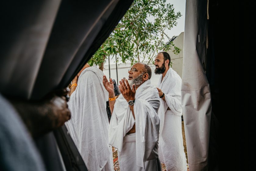 A group of men in white robes participate in a spiritual prayer outdoors, embracing cultural and religious traditions.